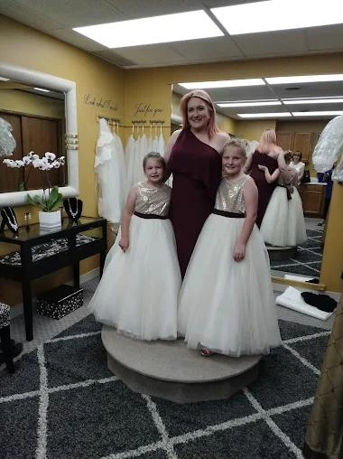 A bridesmaid in a burgundy dress with two flower girls in ivory tulle skirts
