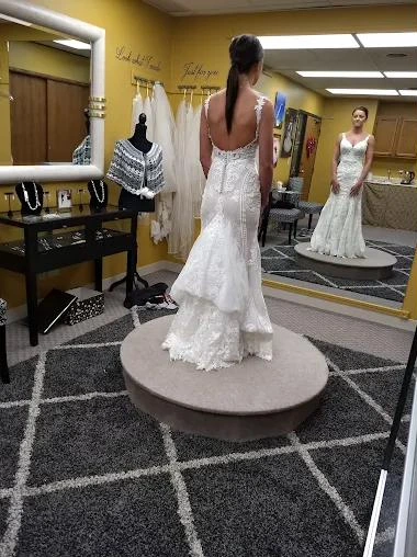 A bride in a lace mermaid gown seen from behind at a fitting, looking into a mirror