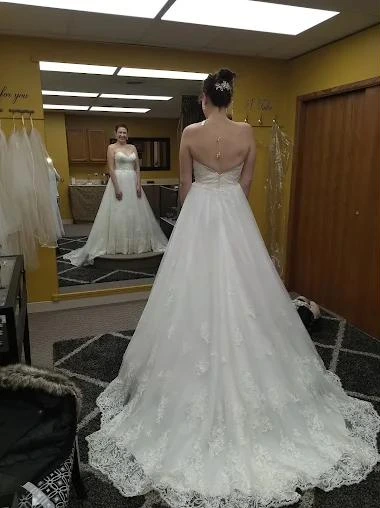 A bride in an A-line gown with a lace-trimmed train, seen from behind in the fitting room