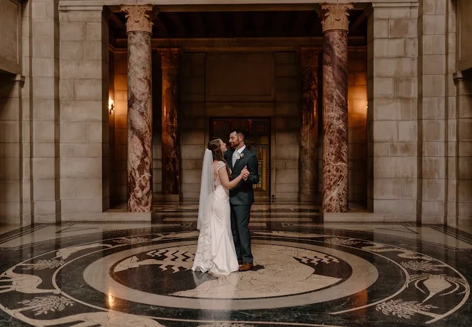 A bride and groom dance in a grand marble hall with tall columns