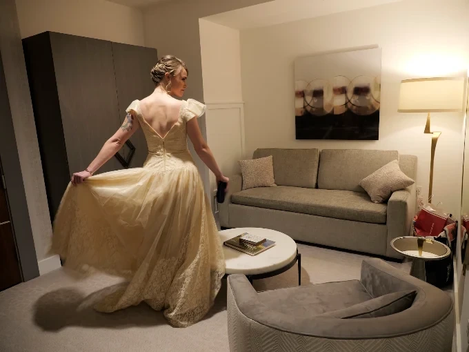 A woman in a vintage cream lace and tulle gown holds out her skirt in a hotel room