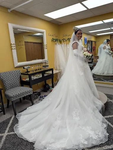 A bride in a lace gown with a long train and veil at the N. Tailor fitting studio
